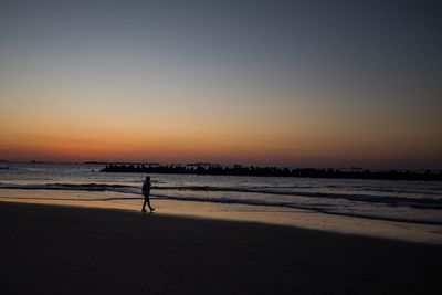 Silhouette man walking on beach against sky during sunset