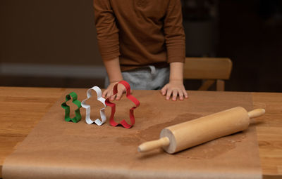 Midsection of boy with rolling pin and cookie cutter on table