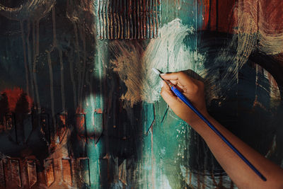 Hand of a female artist holding paintbrush working on canvas