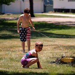 Water spraying on shirtless boy with sister in yard