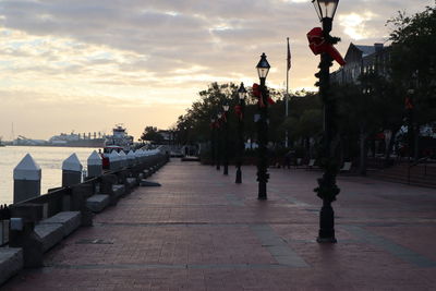 Footpath amidst street against sky during sunset