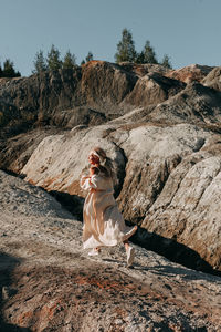 A young blonde girl in a white cardigan runs in the summer along a mountainous brown area