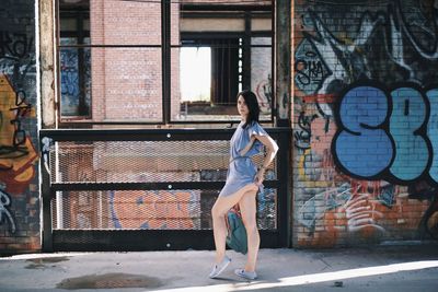 Full length of woman standing against graffiti wall