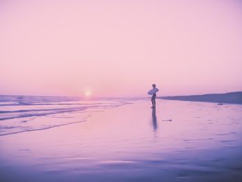 Silhouette man standing on shore against sky during sunset