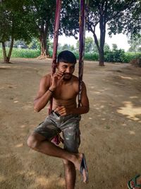 Full length of shirtless boy on swing at playground