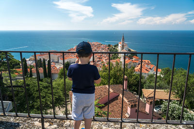 Rear view of man standing by railing against sea