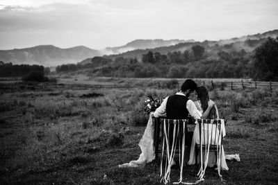 Rear view of newlywed couple sitting on chairs against mountains