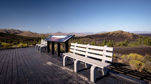 Empty bench on hill against clear blue sky