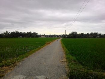 Road passing through field against cloudy sky