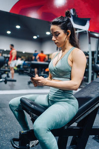 Side view of young woman using mobile phone while sitting in gym