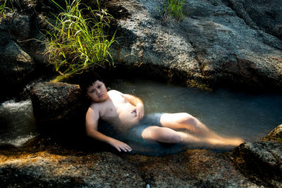 High angle view of shirtless boy on rocks at shore