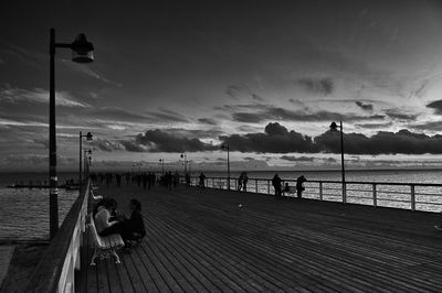 People on pier over sea against sky