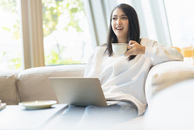 Young woman using phone while sitting on sofa