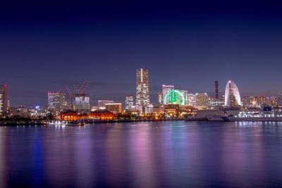 Illuminated city by river against sky at night