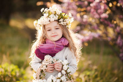 Portrait of cute girl holding flowers standing at park