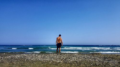 Rear view of man standing on beach against clear sky