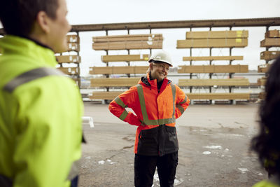 Smiling female worker in reflective clothing standing with colleagues at factory