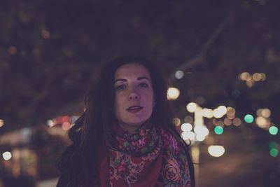 Portrait of woman standing against illuminated lights at night