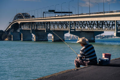 Man sitting on bridge over river against sky