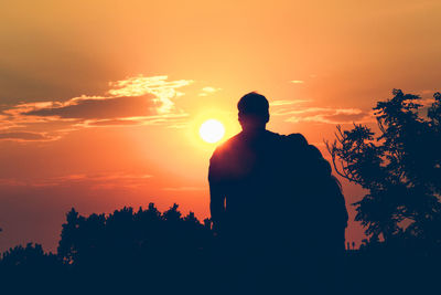 Rear view of silhouette man standing against orange sky