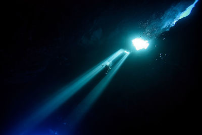 Low angle view of sunlight falling on silhouette person scuba diving undersea