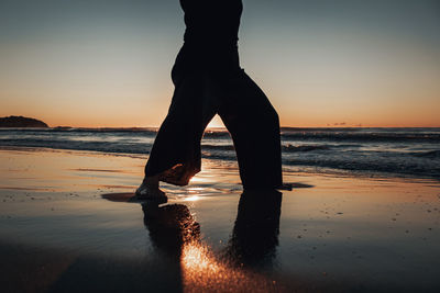 Low section of woman on beach against sky during sunrise