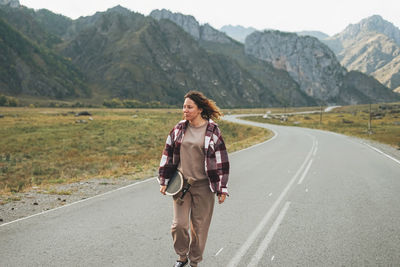 Young woman on skateboard on road against the beautiful mountain landscape, chemalskiy tract, altai