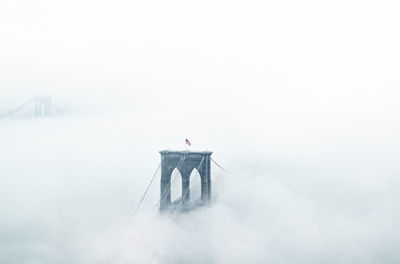 People on suspension bridge in foggy weather against sky