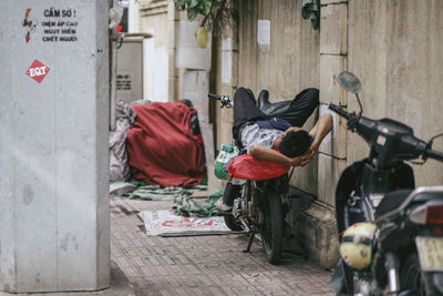 Homeless man sleeping on motorcycle at footpath