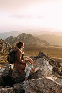 Man sitting on rock looking at mountains against sky