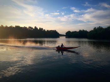 Man on boat in lake against sky during sunset