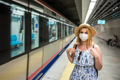 Portrait of woman wearing mask while standing at railroad station platform