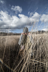 Woman in warm clothes sitting on field against sky