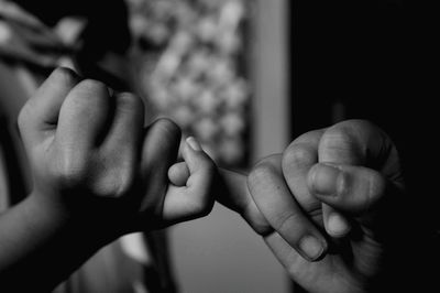 Close-up of parent and daughter doing pinky promise at home