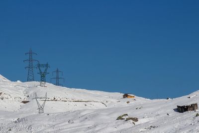 Electricity pylon on snow covered landscape against clear blue sky