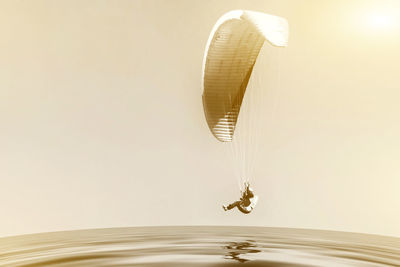 Side view of person paragliding over sea against sky