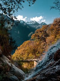 Flowing water over bridge by trees on mountain against sky