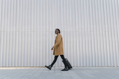 Full length portrait of young man standing against wall in city