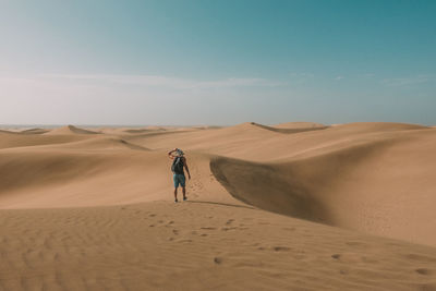 Rear view of man walking on desert against sky
