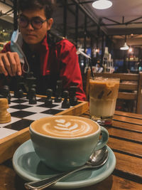 Close-up of coffee cup with man playing chess in background