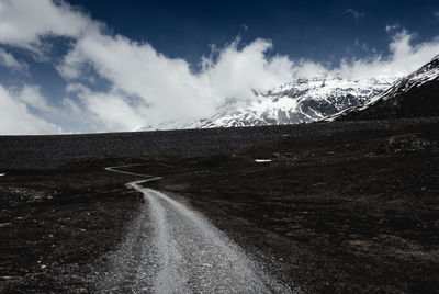 Empty road amidst landscape leading towards snowcapped mountains