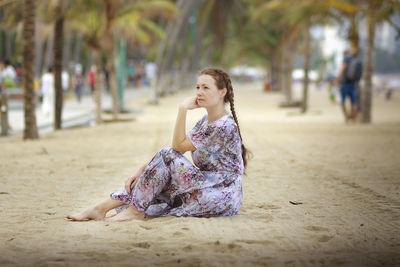 A girl on a sandy beach between an alley of palm trees