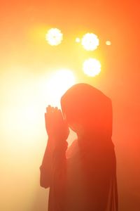 Rear view of silhouette woman standing against orange sky