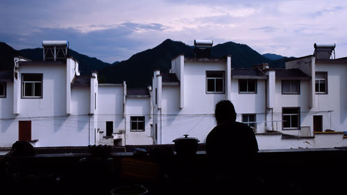 Rear view of silhouette man standing outside house against sky