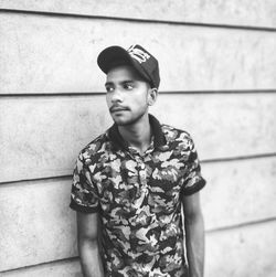 Young man looking away while standing against wall