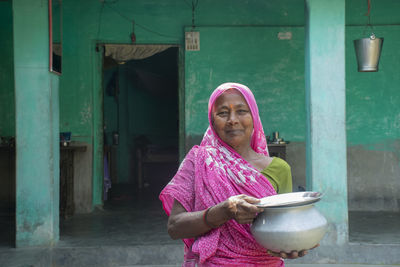 Portrait of smiling woman wearing sari holding kitchen utensils in her hand