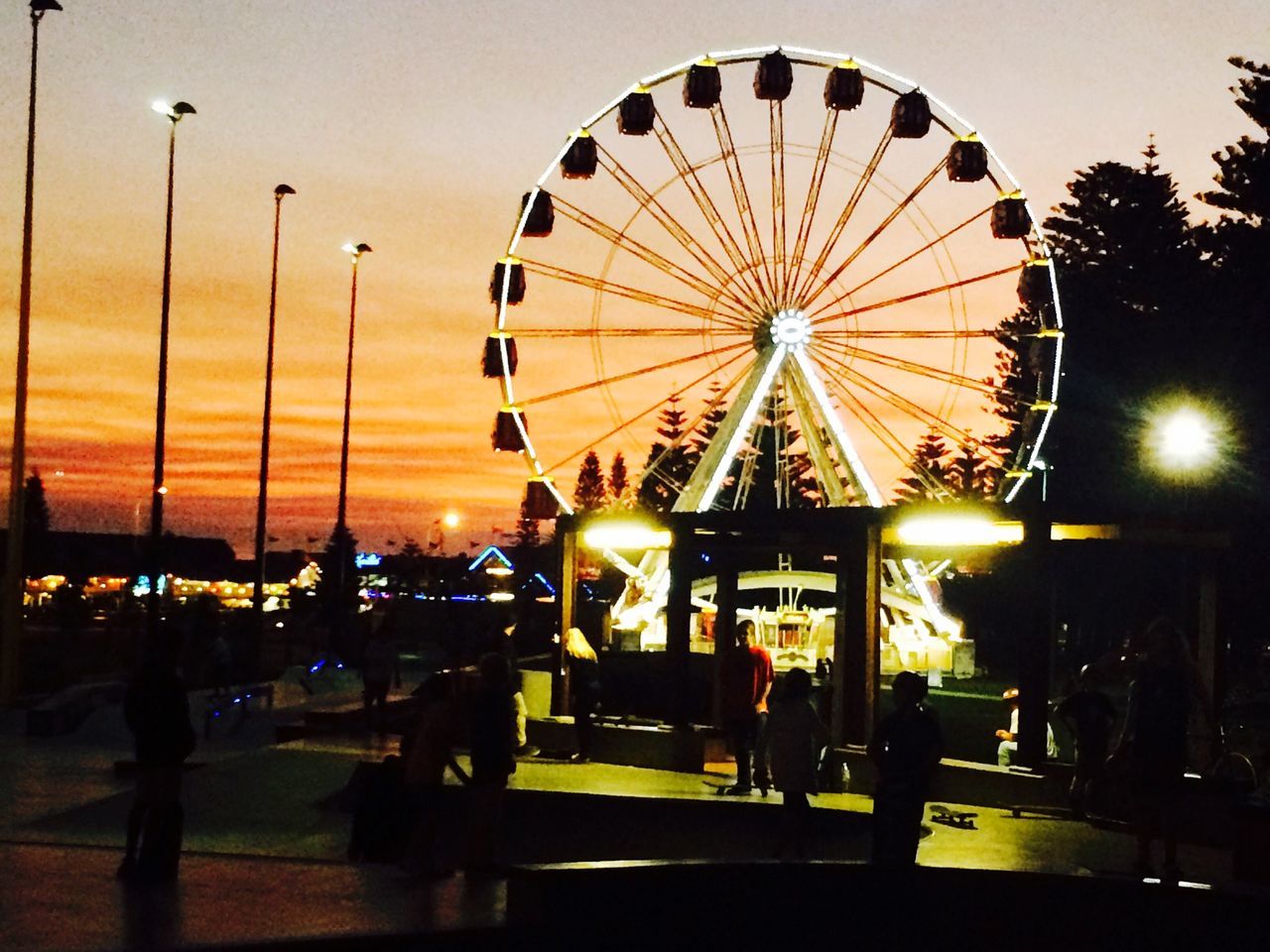 amusement park, amusement park ride, arts culture and entertainment, ferris wheel, sky, sunset, illuminated, leisure activity, silhouette, incidental people, enjoyment, fun, dusk, low angle view, built structure, outdoors, large group of people, cloud - sky, lifestyles