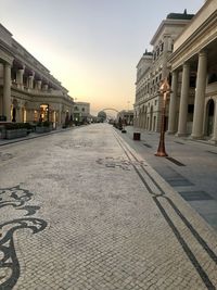 Empty street amidst buildings against sky during sunset