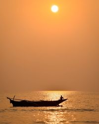 Silhouette man in boat on sea against orange sky