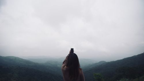 Rear view of woman photographing sky from mountain peak